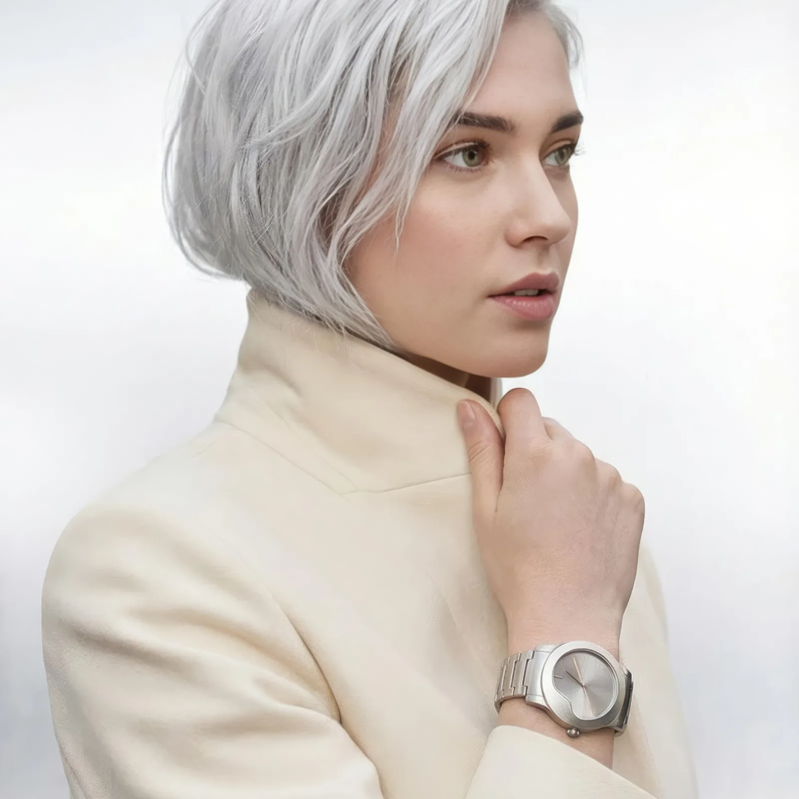 Silver haired model in a cream coat wearing a minimalist steel watch on her wrist