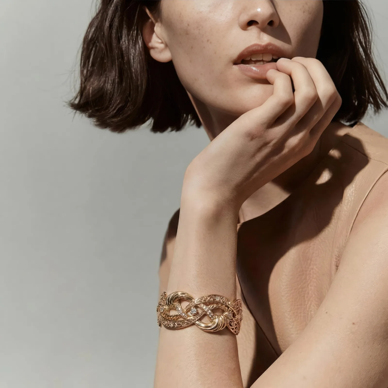 Close up of a woman wearing an ornate gold bracelet with her hand raised to her chin