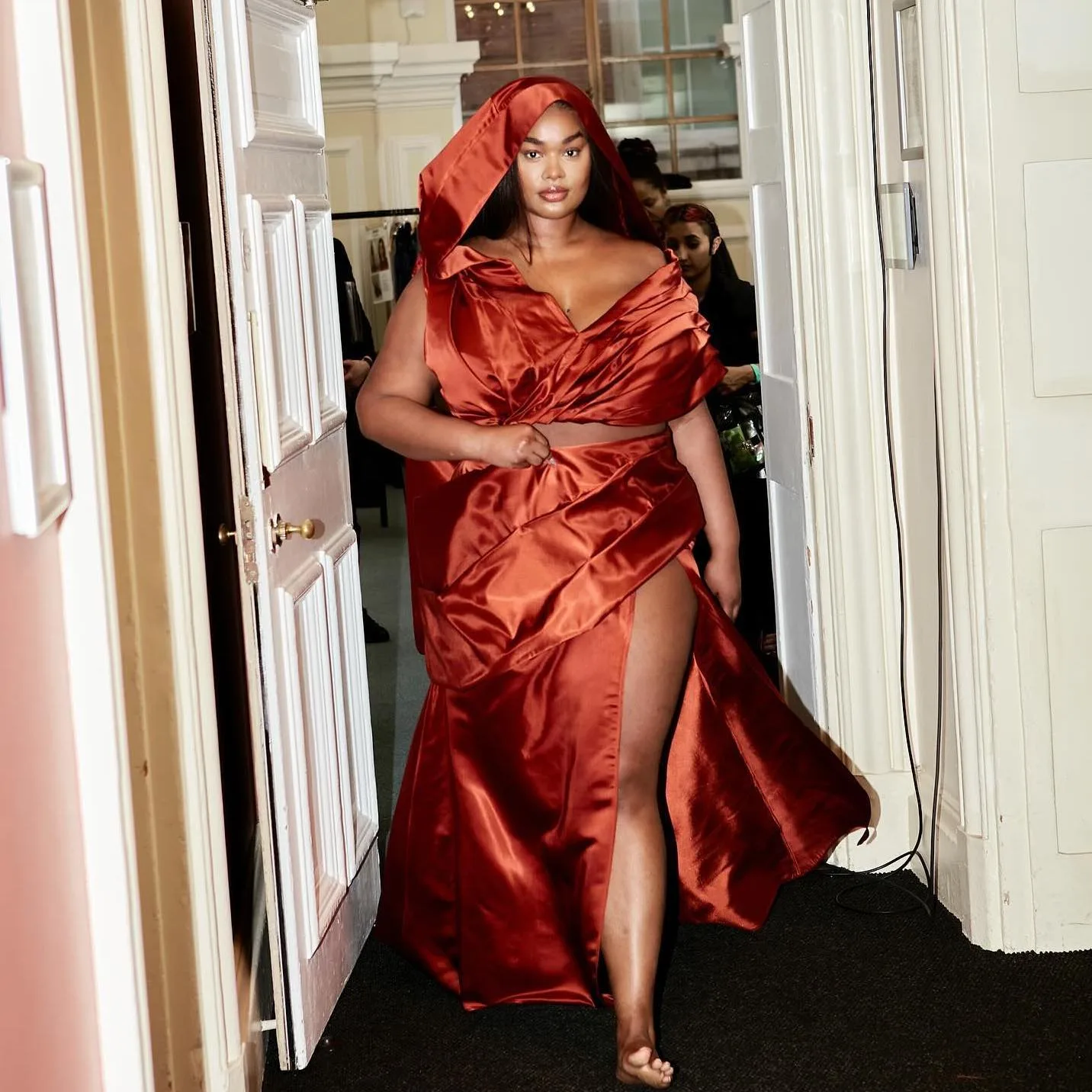 A model backstage at London Fashion Week in a red satin hooded top and matching high slit skirt