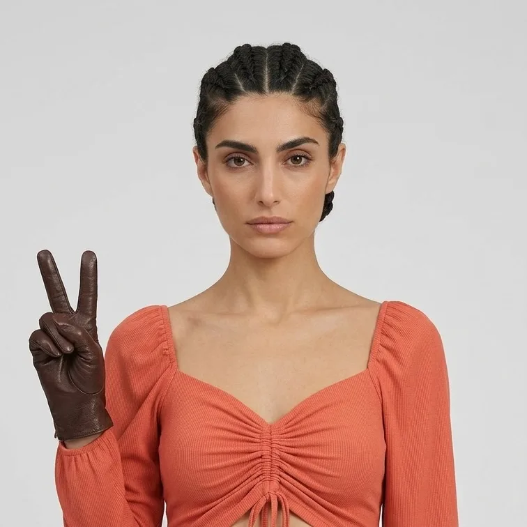 Woman in an orange ruched top raising a brown leather gloved hand in a peace sign