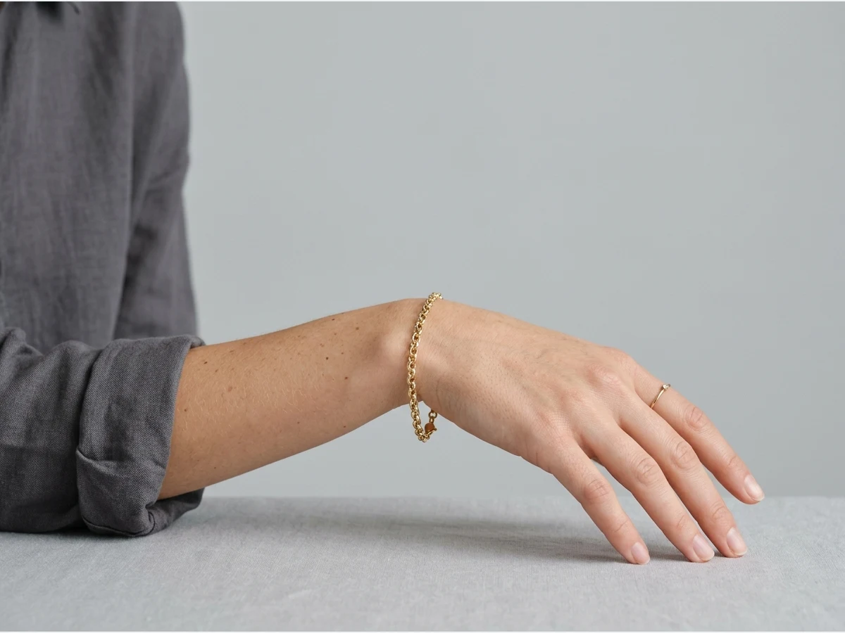 a model photographed to show a bracelet on the wrist, a hand resting, chain bracelet