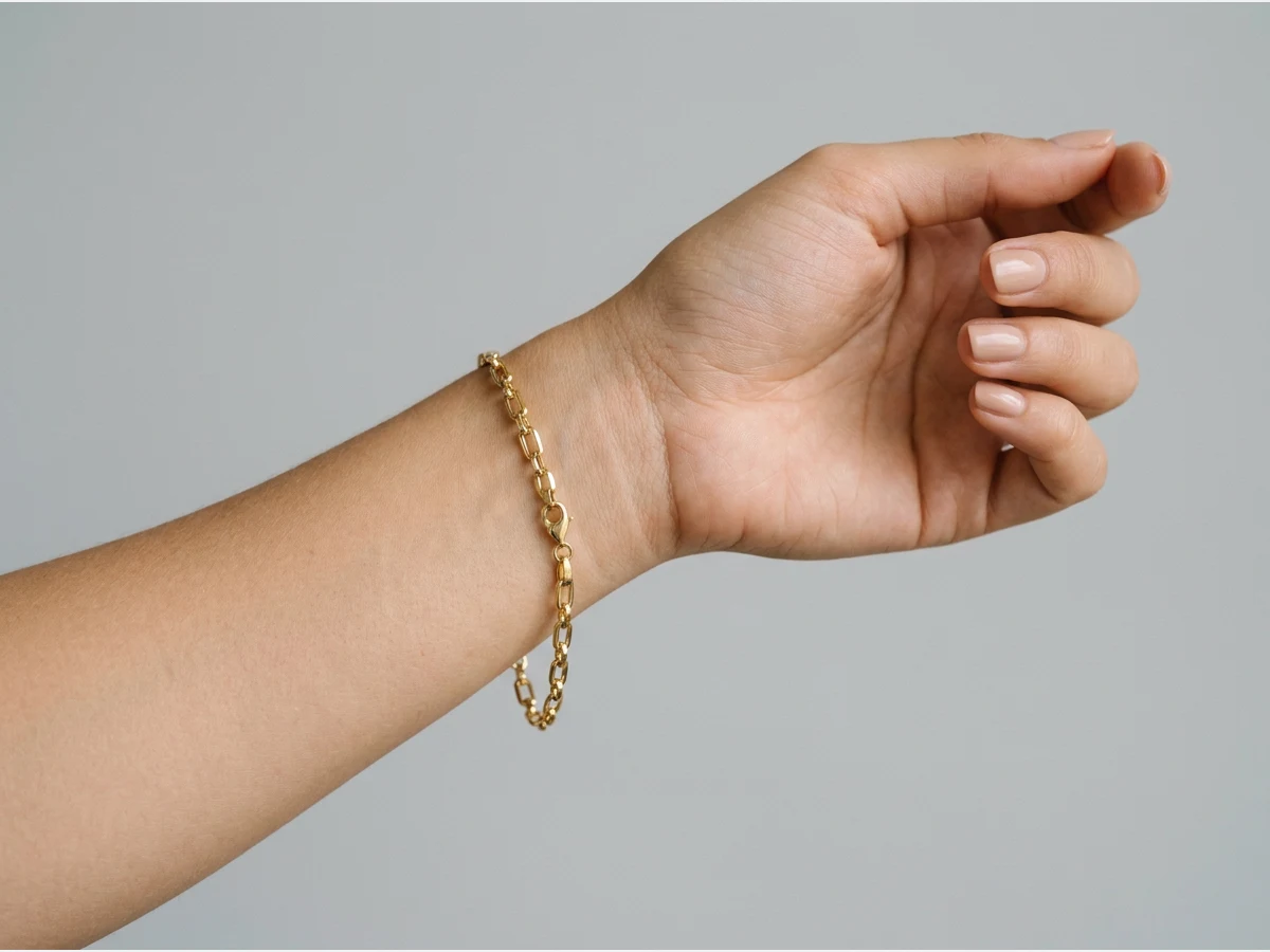 a close shot of a wrist wearing a bracelet, a gold chain bracelet