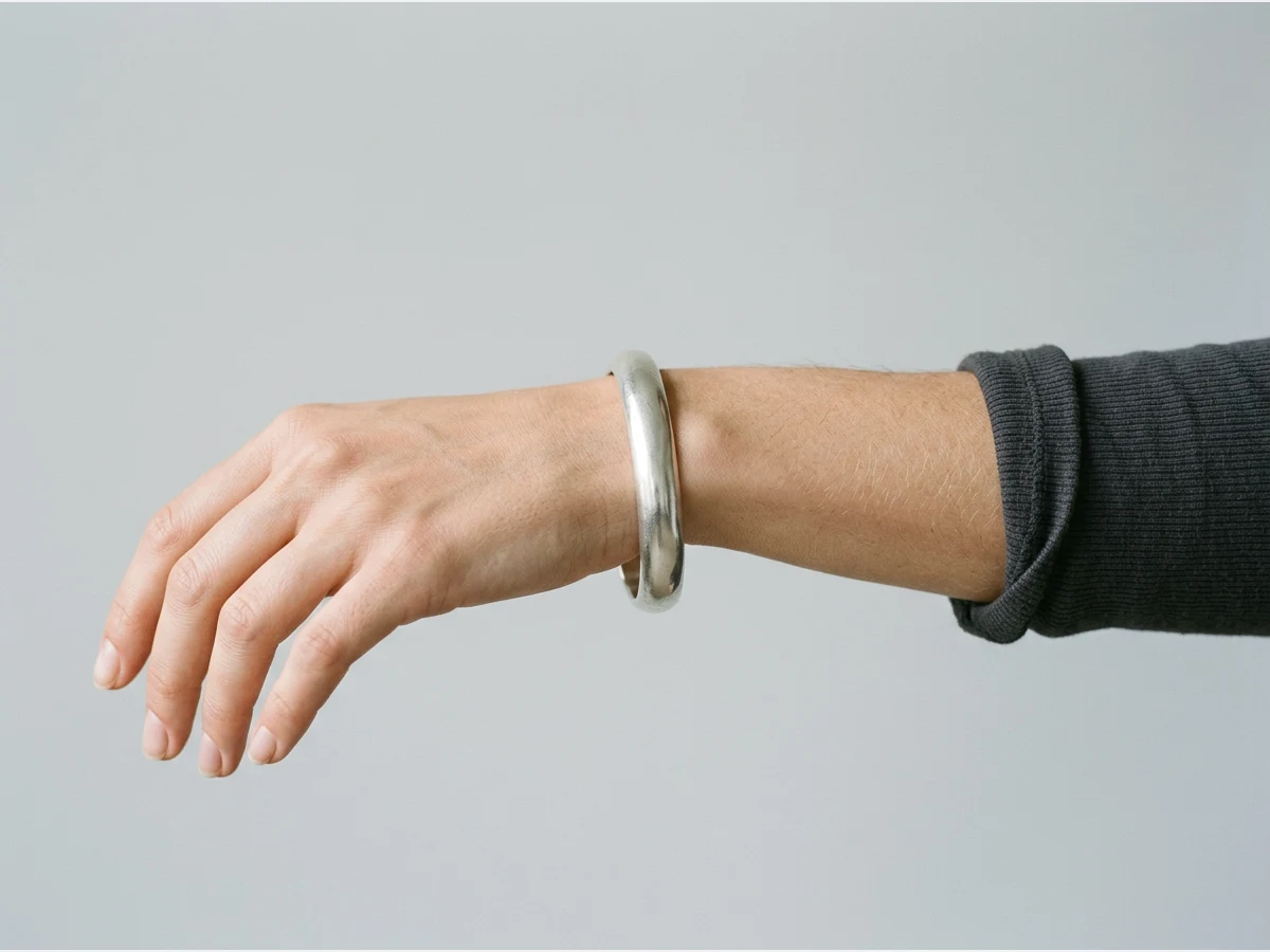 a close shot of a wrist wearing a bracelet, a silver cuff