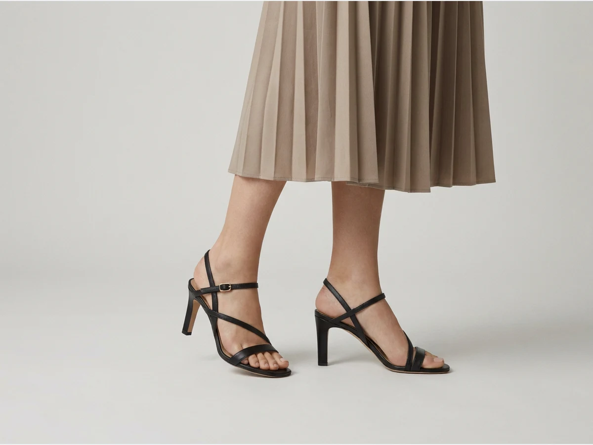 a model's legs and feet wearing designer shoes, heeled sandals with a midi skirt