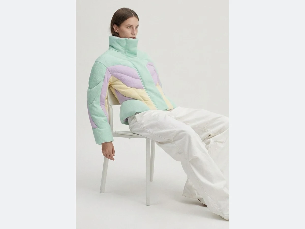 The same model placed in a new scene, seated in a grey studio, full length